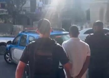 Um dos candidatos a soldado da PM que tinham mandado de prisão em aberto sendo levado para a delegacia Reprodução/Polícia Militar