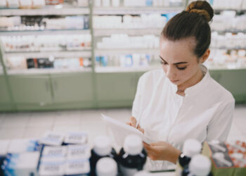 Medicine, pharmaceutics, health care and people concept. Female pharmacist taking medications from the shelf.