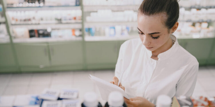 Medicine, pharmaceutics, health care and people concept. Female pharmacist taking medications from the shelf.