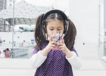 Criança mexe em um smartphone enquanto ouve música com fones de ouvido — Foto: Anne-Sophie Bost/AltoPress/PhotoAlto