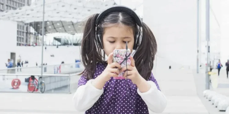 Criança mexe em um smartphone enquanto ouve música com fones de ouvido — Foto: Anne-Sophie Bost/AltoPress/PhotoAlto